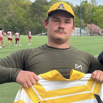 Hunter Poturaj in an App State cap holding a jersey with the number 2.