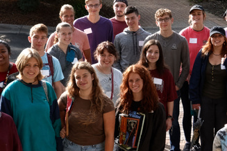 Group standing outdoors on a paved area in bright daylight.