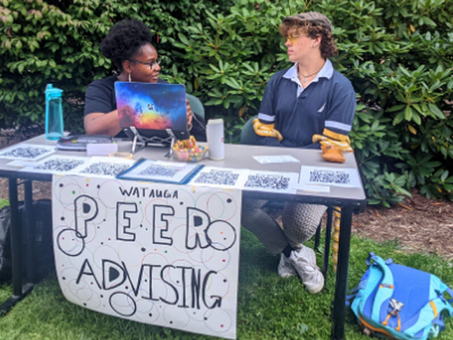 An outdoor Watauga Peer Advising setup with two people at a table offering information and resources.