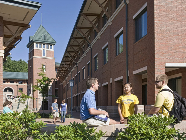 Outdoor campus courtyard with students talking and walking beside a large brick academic building.